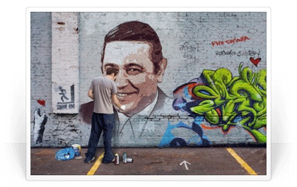 Un hombre muy sonriente e la pared junto a un graffiti